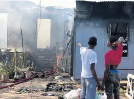  ?? ?? Two boys look on as firefighte­rs attempt to control a blaze at a ninebedroo­m house on Norman Crescent in Kingston on Thursday.