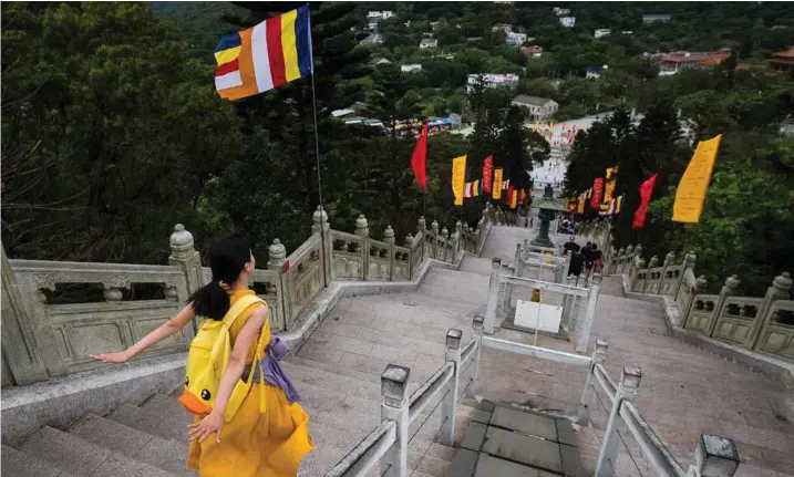  ??  ?? A woman glides down the stairs leading to the Tian Tan Buddha statue in Hong Kong.