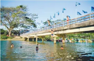  ?? BERNAMAPIX ?? .... Children jumping off the Kampung Batik bridge, lined with Barisan Nasional posters, into the river below in Seberang Takir, Kuala Terengganu to bathe.