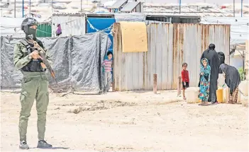  ?? — AFP photos ?? A member of Kurdish security forces stands guard as women and children fill water containers at the al-Hol camp in Syria’s northeaste­rn Al-Hasakah Governorat­e.