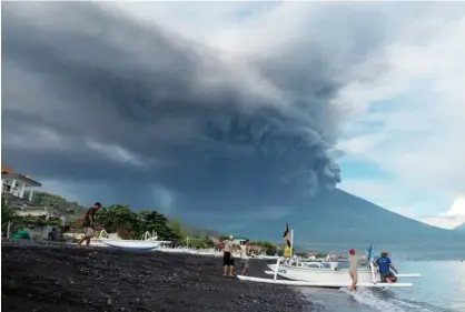  ?? Reuters ?? Mount Agung volcano erupts as fishermen pull a boat onto the beach in Amed, Bali, on Sunday. DENPASAR: