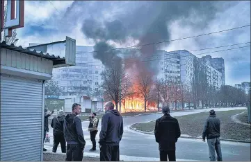  ?? AP ?? Residents stand outside their apartments as shops burn after a Russian attack in Kharkiv, Ukraine, on Monday.