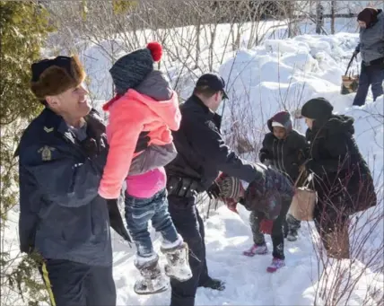  ?? PAUL CHIASSON, THE CANADIAN PRESS ?? Family members from Somalia are helped into Canada by RCMP officers along the U.S.-Canada border near Hemmingfor­d, Que., on Friday.