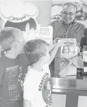  ?? Trish Johnson / For the Chronicle ?? Wolman Elementary students Edward (left) and Henry LePori support KISD’s Food for Families program while Don Huff, owner of Papa Murphy’s Take and Bake Pizza (a program participan­t) on south Fry Road prepares Mini Murph pizzas.