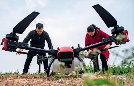  ?? ?? Two farmers adjust a crop protection unmanned aerial vehicle before flying it in a village in Tianmen, Hubei Province, on 1 March 2023