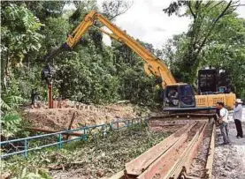  ?? (Foto BERNAMA) ?? Jentera melakukan kerja pemasangan kepingan besi menghadang pergerakan tanah di tebing anak Sungai Sering.