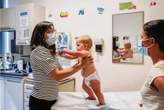  ?? Photos by Brontë Wittpenn/The Chronicle ?? Pediatrici­an Nicole Glenn speaks with Lucy’s mother, Geri Landman, while helping then-14-month-old Lucy stand during a check-up at Sutter Health in August.