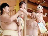  ??  ?? Sumo wrestlers hold up crying babies during a “Baby-cry Sumo” event.