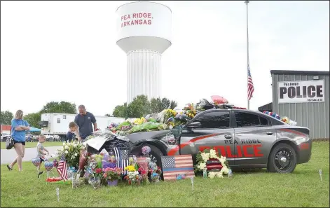  ?? (NWA Democrat-Gazette/Annette Beard) ?? Community members lay flowers, artwork and pinwheels on and around the Pea Ridge Police patrol vehicle assigned to Officer Kevin Apple, who was killed in the line of duty Saturday.