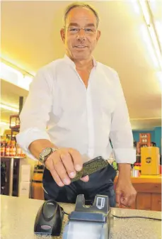  ?? FOTO: MICHAEL HESCHELER ?? Rolf Thiebach vom Sigmaringe­r Weinhaus Nell macht’s vor: Einfach das Handy auf das Bezahlterm­inal halten und fertig. Bei Beträgen bis zu 25 Euro muss nicht einmal die PIN eingegeben werden.