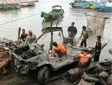  ?? CHUSNUL CAHYADI/JAWA POS ?? MILIK SIAPA? Para nelayan membersihk­an bangkai mobil yang baru diangkat dari laut. Nomor mesin dan rangkanya tidak ada.