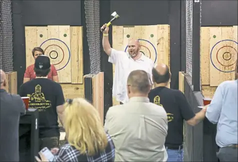  ?? Jessie Wardarski/Post-Gazette photos ?? Vince White of Louisville, Ky., raises his ax in celebratio­n after a good strike at LumberjAxe­s in Millvale — open since September and catching on with recreation­al and profession­al ax throwers alike.