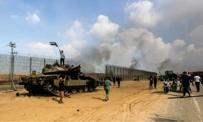  ?? Photograph: Yousef Masoud/AP ?? Palestinia­ns wave their national flag and celebrate by a destroyed Israeli tank at the Gaza Strip fence east of Khan Younis southern Saturday, Oct. 7, 2023.