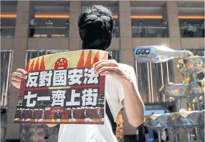  ??  ?? LEFT
A pro-democracy protester holds a placard that reads ‘Against the national security law. March on July 1’ during a protest in Hong Kong.