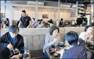  ?? Mariah Tauger For The Times ?? DINERS dig in at Hangari Bajirak Kalgooksu, where a line forms for thick, hand-cut noodles served in anchovy-scented broth with Manila clams. As prelude, a tiny bowl of barley arrives.