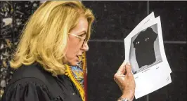  ??  ?? Judge Laura Johnson holds photos of the bullet-punctured shirt Kunta Kinte Riddick was wearing when he was shot Nov. 29, during a “stand your ground” hearing Thursday in Samuel “Bo” Barber’s first-degree murder case, subsequent­ly dismissed Friday.