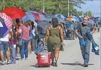  ?? Matias J. Ocner/Miami Herald via AP ?? Cecil Umana, 64, walks past hundreds of people who are in line hoping to receive aid from a post-hurricane disaster center outside of Tropical Park on Sunday in West Miami-Dade, Fla.