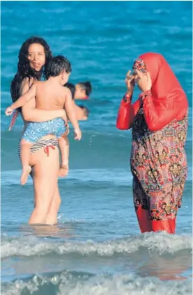  ?? AFP ?? Una mujer vestida con un burkini y otra con bikini disfrutan un baño en las aguas del mar Mediterrán­eo, en una playa en Túnez.
