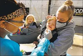  ?? Carolyn Cole Los Angeles Times ?? KRISTEN HUDSON holds son Liam, 21⁄2 , as he gets tested for the coronaviru­s in Santa Monica. He must have a negative test before starting preschool.