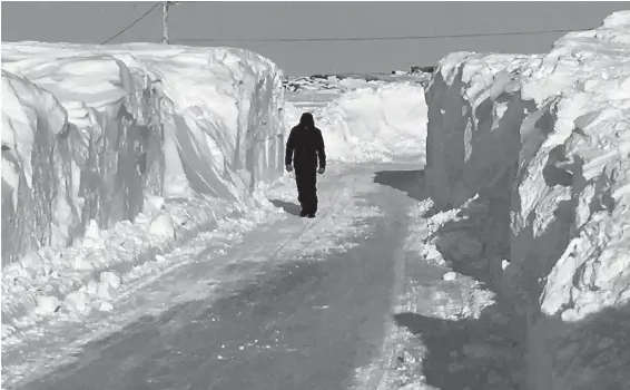  ??  ?? A Churchill, Man., resident walks down a plowed street on Saturday after an “unpreceden­ted” blizzard left nine-metre snowdrifts in some parts of town.