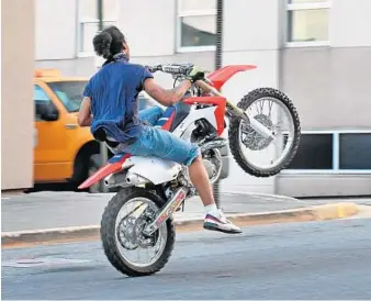  ?? KENNETH K. LAM/BALTIMORE SUN ?? A dirt bike rider does a wheelie westbound on Madison Street toward North Calvert Street. Baltimore police have been cracking down on dirt bikers who ride on city streets.