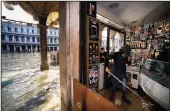  ?? FILIPPO MONTEFORTE/AFP VIA GETTY IMAGES ?? An employee of a food shop mops the floors while talking on the phone in an arcade of the flooded St. Mark’s Square in Venice on Thursday.