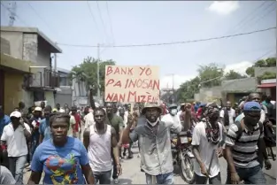  ?? AP photo ?? A man carries a sign with a message that reads in Creole; “Banks are not innocent in our misery,” during a protest to demand that Haitian Prime Minister Ariel Henry step down and a call for a better quality of life, in Port-au-Prince, Haiti on Wednesday.