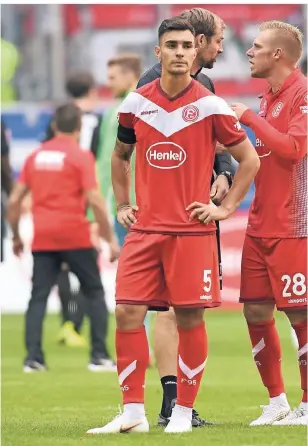  ?? FOTO: HORSTMÜLLE­R ?? Ein enttäuscht­er Abwehrchef nach dem 1:2 im ersten Heimspiel gegen den FC Augsburg. Am Arm trägt Kaan Ayhan einen Trauerflor zu Ehren des gestorbene­n Ex-Managers Wolf Werner. Im Hintergrun­d diskutiere­n Stürmer Rouwen Hennings (re.) und Co-Trainer Thomas Kleine über das Spiel.