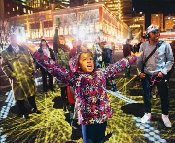  ?? Rebecca Droke/Post-Gazette ?? Amariya Bledsoe, 9, of Elliott interacts Friday with the art installati­on “Congregati­on” in Market Square. Lights are projected into the square and, as people interact with the lights, their interactio­ns are projected on a screen.