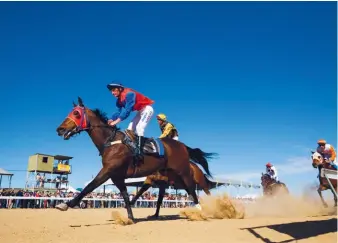  ??  ?? Horses gallop to the finishing line on the sandy straight under a sweltering sun