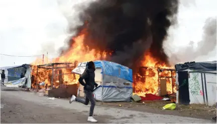  ??  ?? A migrant runs next to a burning makeshift shelter at the “Jungle” migrant camp in Calais, France, on Wednesday. (AFP)