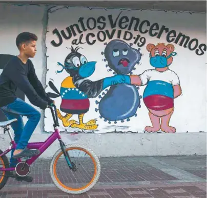  ?? / AFP ?? Un joven venezolano en una calle de Caracas pasa frente a un grafiti que invita a derrotar “unidos” el virus.
