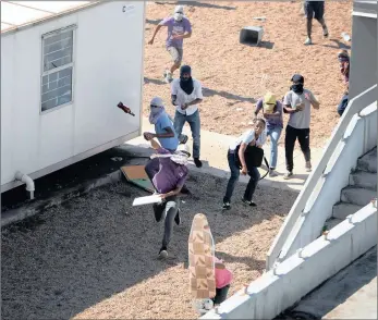  ?? PICTURE: MOTSHWARI MOFOKENG ?? Protesters hurl beer bottles and rocks while one protester takes cover behind an ironing board during protests at the UKZN Westville campus yesterday.