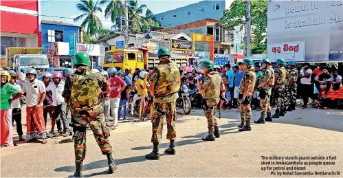  ?? ?? The military stands guard outside a fuel shed in Ambalantho­ta as people queue up for petrol and diesel
Pic by Rahul Samantha Hettiarach­chi