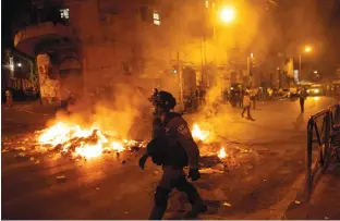  ?? ( Ronen Zvulun/ Reuters) ?? A POLICEMAN patrols near burning garbage during an operation to enforce pandemic- related restrictio­ns, in Jerusalem’s Mea She’arim neighborho­od, earlier this month.