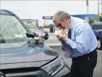  ?? Ted Shaffrey/Associated Press ?? A man with a face mask and glove eats a hamburger on the hood of his car Friday because the dining room is closed at a rest stop along Interstate 95 in Sewaren, N.J., during the coronaviru­s pandemic.