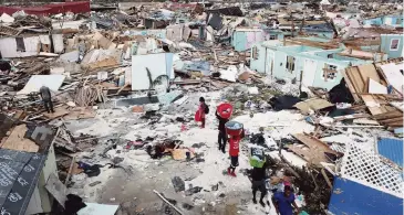  ?? AL DIAZ adiaz@miamiheral­d.com ?? People walk amid the destructio­n from Hurricane Dorian in an area called The Mudd in Marsh Harbour on Great Abaco Island in the Bahamas on Thursday.