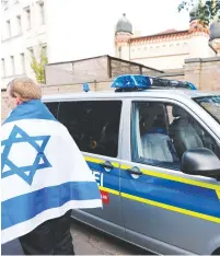  ?? (Fabrizio Bensch/Reuters) ?? A MAN WEARING AN ISRAELI FLAG is seen next to a police vehicle outside the synagogue in Halle, Germany yesterday, after two people were killed in a shooting.