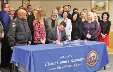  ?? PROVIDED ?? Ulster County Executive Pat Ryan, seated, signs the county’s 2020 budget on Thursday, Dec. 12, in the Esopus Town Hall, surrounded by county legislator­s, elected county officials and others.