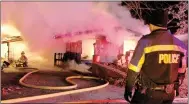  ?? Keith Bryant/The Weekly Vista ?? Bella Vista Firefighte­r-Paramedic William Coker, far left, background, sprays the burning house on Ciemny Lane Tuesday, Dec. 6, while Bella Vista police officer J.D. Jordan stands by.