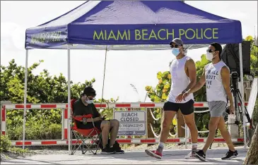  ?? LYNNE SLADKY / ASSOCIATED PRESS ?? People pass a closed entrance to the beach Friday in the South Beach neighborho­od of Miami Beach, Florida. Beaches in South Florida are closed for Fourth of July weekend to avoid further spread of the coronaviru­s.