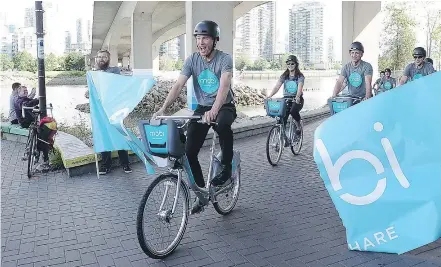  ?? NICK PROCAYLO/PNG ?? Vancouver Mayor Gregor Robertson smiles as he rides a shared bike through a banner Wednesday at False Creek when the city and Vancouver Bike Share launched its Mobi program.