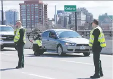  ?? WAYNE CUDDINGTON ?? Unmasked Sûreté du Québec officers stop vehicles on the MacdonaldC­artier Interprovi­ncial Bridge as they enter Gatineau from Ottawa to check for occupants possibly infected with COVID-19.
