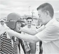  ?? ?? KEMAS: Ding memakaikan topi keledar kepada seorang penunggang motosikal pada program Kempen Kesedaran Keselamata­n Jalan Raya sempena Hari Gawai di Sarikei.