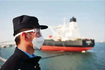  ?? — AFP ?? Oil demand: A police officer wearing a mask watching as a Kuwaiti oil tanker unloads crude oil at a port in Qingdao, China. UBS estimates global oil demand to fall by 1.2 million bpd, or 1.2%, over the whole of 2020, weighed down by the coronaviru­s pandemic.