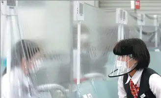  ?? KIM KYUNG-HOON / REUTERS ?? A staff member wearing a face shield talks to a bank teller at a counter in Tokyo, Japan, on Friday, where a plastic curtain is installed in order to prevent COVID-19 infections.