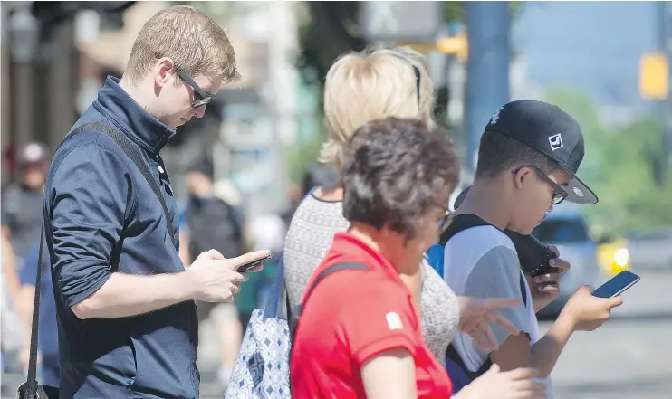  ?? GERRY KAHRMANN/PNG FILES ?? People look at their smartphone­s while waiting to cross Burrard at Robson streets last Friday. Some officials want distracted walking regulated.