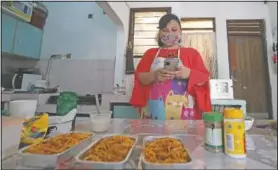  ??  ?? Rani Nurwitawat­i checks her mobile phone as she prepares food for her online customers at her home in Bekasi.