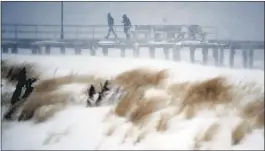  ?? JULIO CORTEZ — THE ASSOCIATED PRESS ?? People walk on a small pier as snow covers the sand dunes during a snowstorm that hit Ocean Grove, N.J., on Thursday. A massive winter storm swept from the Carolinas to Maine on Thursday. Blizzard warnings and states of emergency were in wide effect,...