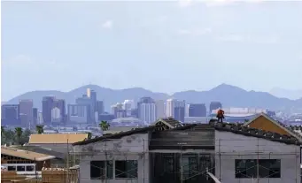  ?? Ap file ?? SPREADING OUT: With the downtown Phoenix skyline in the background, a roofer works on a home being built in a new housing developmen­t as expansive urban sprawl continues in Arizona.